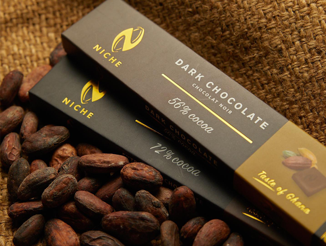 Niche brand dark chocolate bars, 56% and 72% cocoa, resting on raw cocoa beans at a Ghana manufacturing facility.