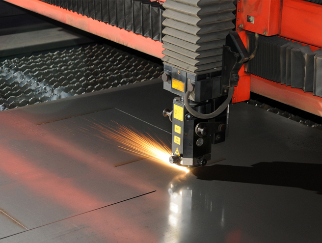Industrial laser cutter slicing through thick metal with sparks flying during contract manufacturing.