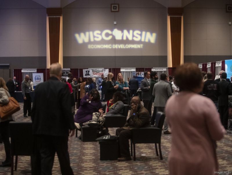 Professionals networking at a business conference beneath a Wisconsin Economic Development projection.