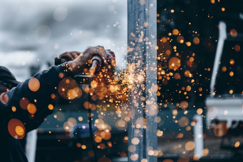 Worker uses an angle grinder to cut metal for Wisconsin manufacturing, producing a spray of orange sparks.