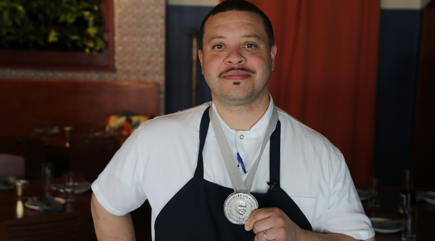 Chef in white uniform and navy apron wearing a James Beard Foundation award medal.