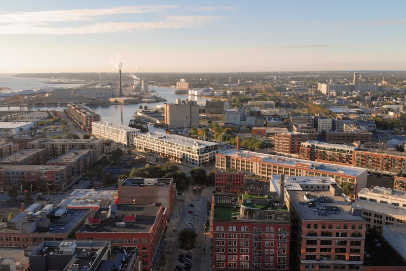 1 Aerial view of a city waterfront featuring industrial buildings, apartment complexes, and a river harbor.
