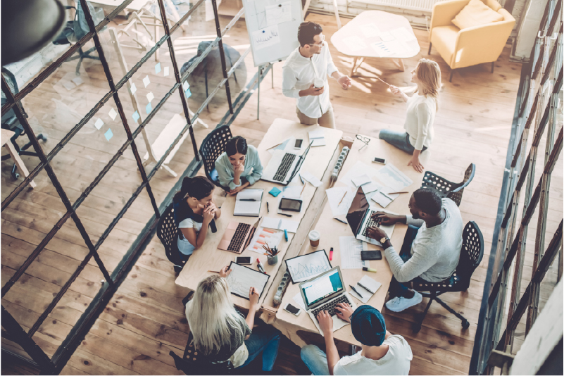 6 Diverse professionals collaborating around a large conference table in a modern open-plan office.